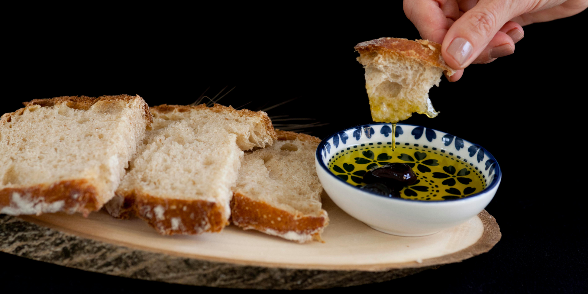 Dipping bread into a small bowl of argan oil on a dark background
