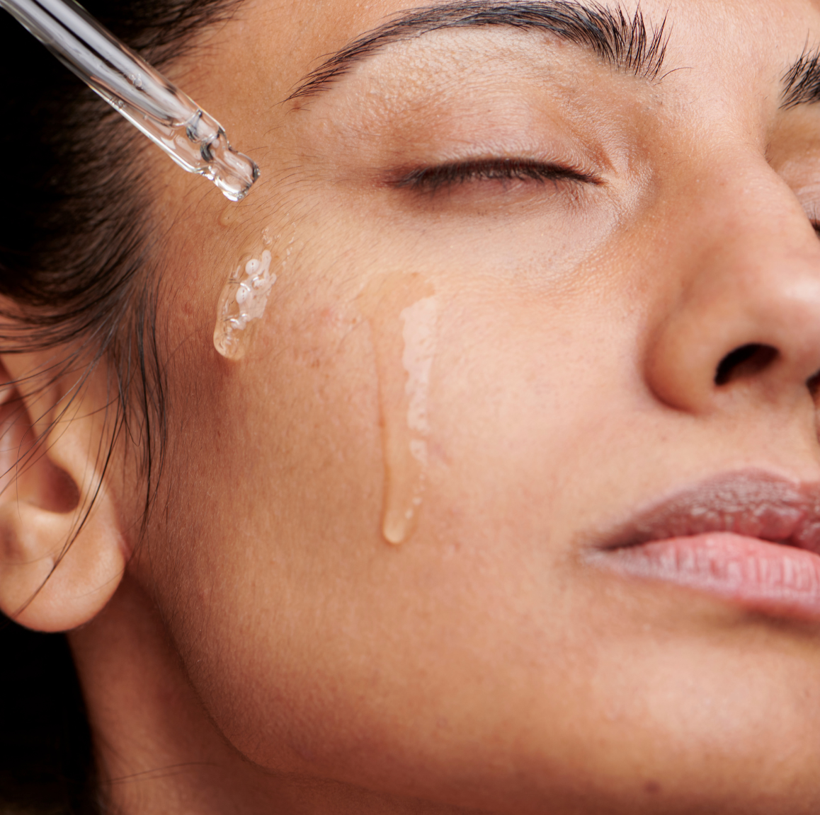 Close-up of a woman applying a skincare product to her face with a dropper.