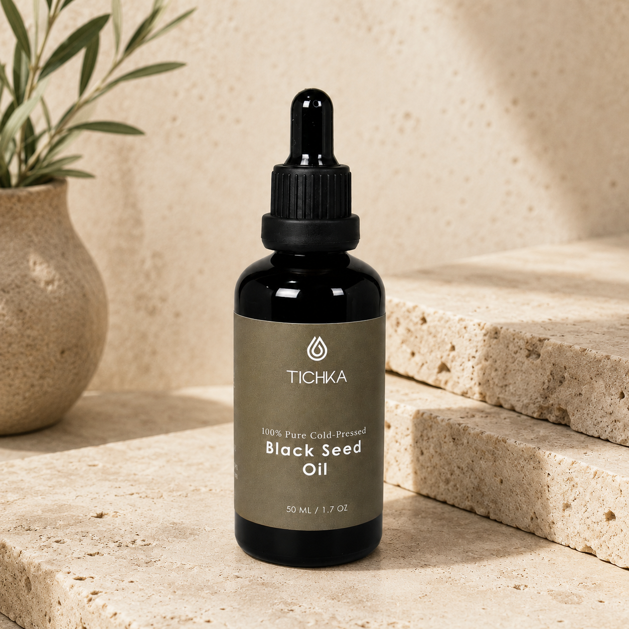 A bottle of Tichka Black Seed Oil on a beige stone surface with a potted plant in the background.