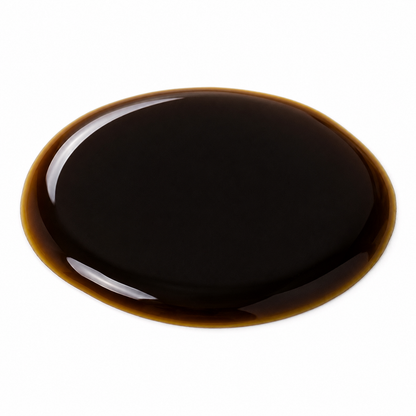 A glossy, dark brown liquid, likely a sauce, syrup, or oil, spread in a circular pool on a solid white background.