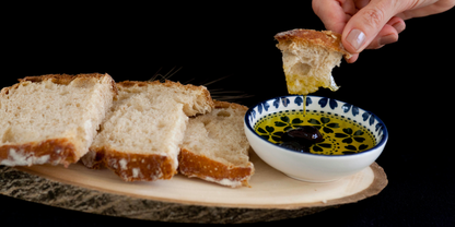 Dipping bread into a small bowl of argan oil on a dark background