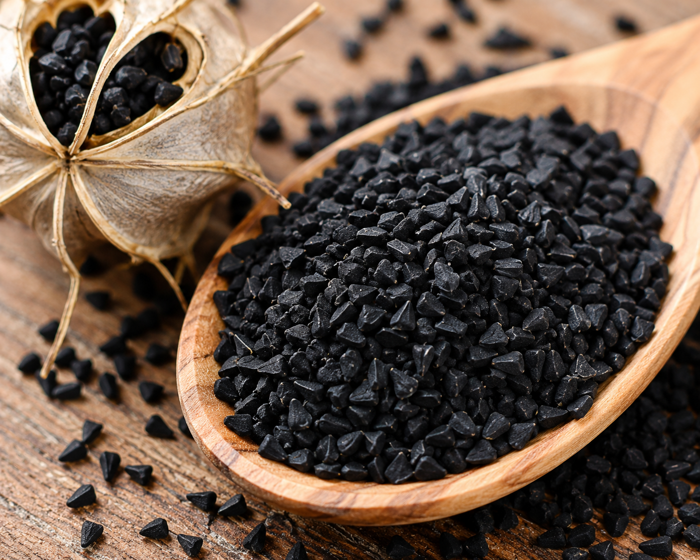 Black carbon granules in a wooden spoon with a dried garlic bulb prop on a rustic wooden surface.