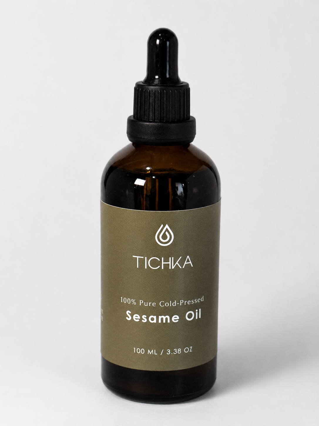 A 100 mL amber glass dropper bottle of Tichka Sesame Oil with a black dropper cap and a muted olive-brown label, set against a light gray background.