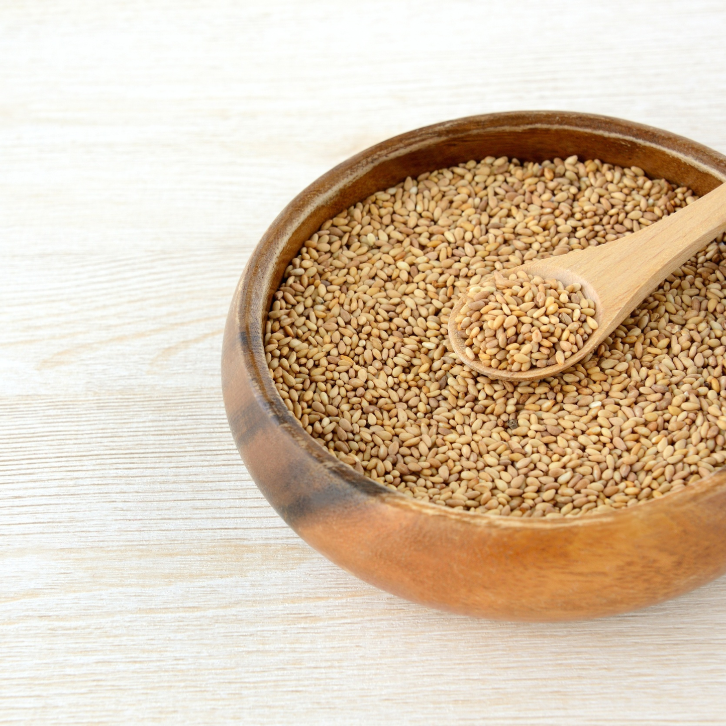 Wooden bowl filled with sesame seeds on a light wooden surface