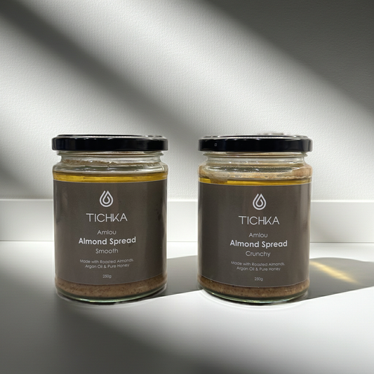 Two jars of TICHKA almond spread on a reflective surface with a gray background